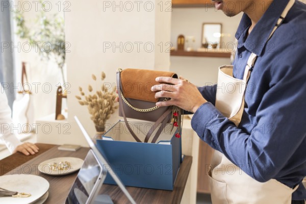 A retail assistant carefully places a stylish handbag into a blue box at a boutique bag store, ensuring customer satisfaction with attentive and personalized service