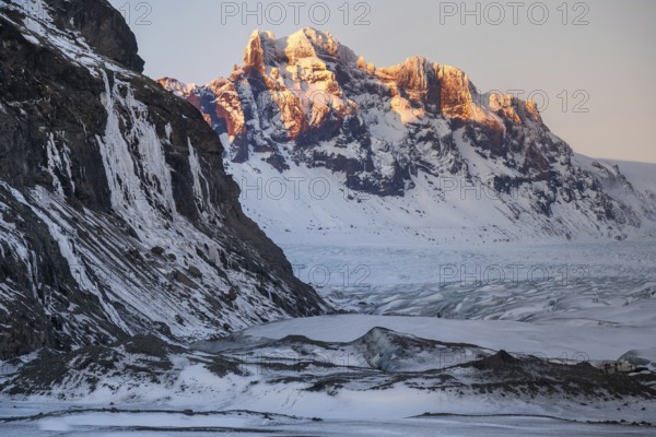 Captivating Icelandic winter scenery with majestic snow-capped mountains in Skaftafell and expansive glaciers illuminated by a delicate sunset, showcasing natural beauty and tranquility