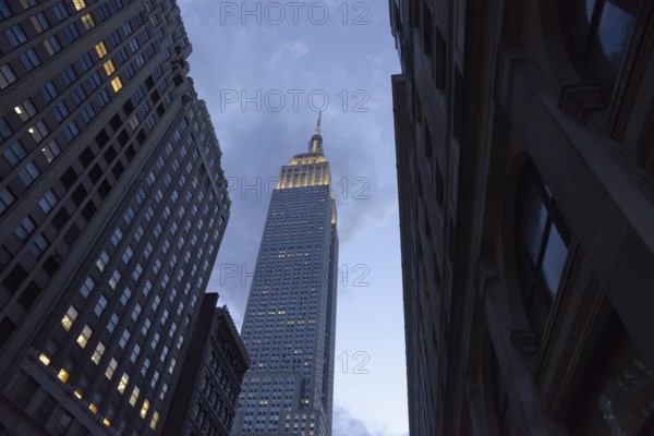 Low angle of the Empire State Building towers majestically between neighboring skyscrapers in Manhattan, highlighted by a fading dusk light
