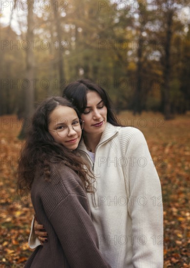 Mother and daughter enjoy a warm embrace amidst the colorful autumn leaves in a serene forest setting, showcasing familial love and tranquility during the fall season