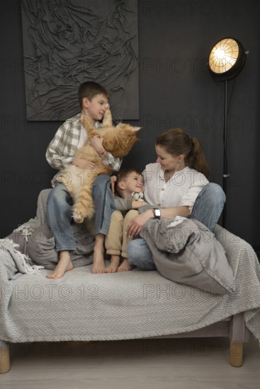 A warm family scene featuring a mother and her two children sharing a joyful moment with their fluffy orange cat. They are seated on a couch in a cozy living room setting