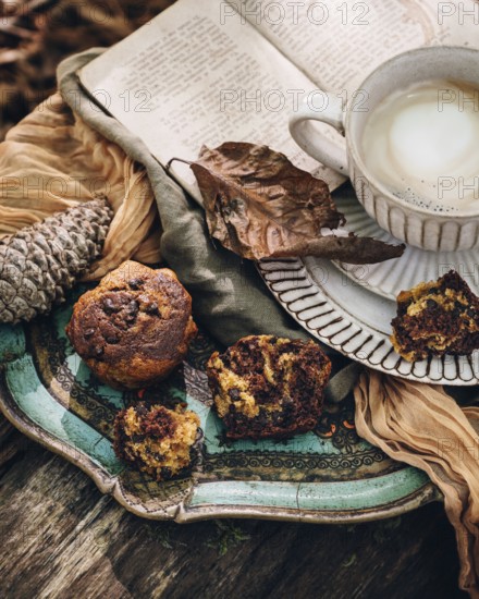 A cozy autumn setting featuring pumpkin muffins, a warm cup of coffee, and an open book. The scene is enriched with rustic elements such as pine cones and fall leaves for a seasonal touch
