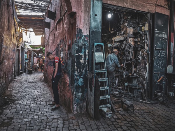 Narrow alley with cobblestones and a workshop, bustling urban atmosphere, small, dark workshop full of cables and metal in the Medina with craftsmen at work, atmospheric lighting, nostalgic atmosphere, Morocco