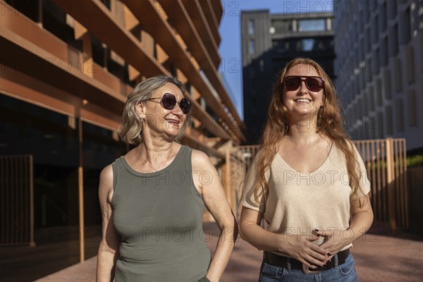 A mom and daughter share a joyful moment outdoors on a sunny day, both wearing sunglasses. The relaxed setting highlights their connection and happiness in each otherâ€™s company