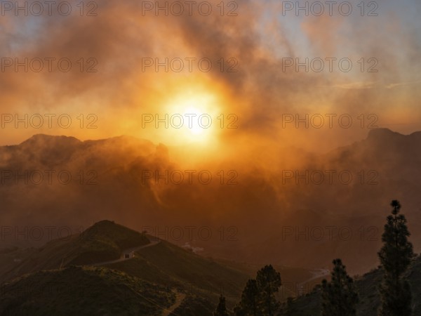 Dramatic sunset lighting up the clouds and mist over the mountains, viewed from Cruz de Tejeda in Gran Canaria, with Roque Nublo in the distance