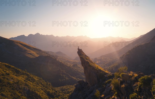 A breathtaking view of a hiker standing on a mountain peak, bathed in the golden light of a sunrise in the Pyrenees. The vast landscape and glowing sky create an inspirational scene in summer