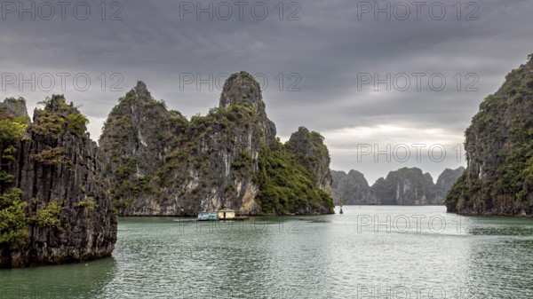 Limestone cliffs and small boats on calm waters under a cloudy sky, The landscape and islands of Halong Bay in Vietnam