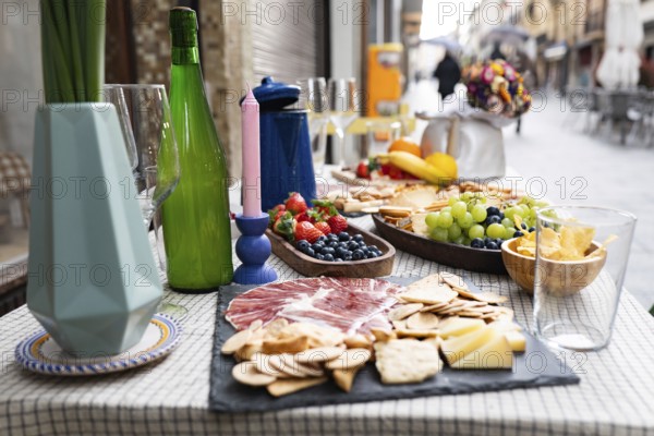 Elegant outdoor dining setup with a delightful charcuterie board, fresh fruit, and beverages. Decorative elements like candles and vases add charm to the street side ambiance
