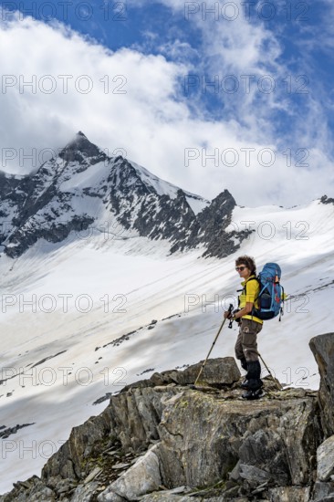 Mountaineer on a rock between snow, descent from the summit of Schönbichler Horn, view of snow-covered and glaciated mountain landscape with summit Großer Möseler, Berliner Höhenweg, Zillertal Alps, Tyrol, Austria