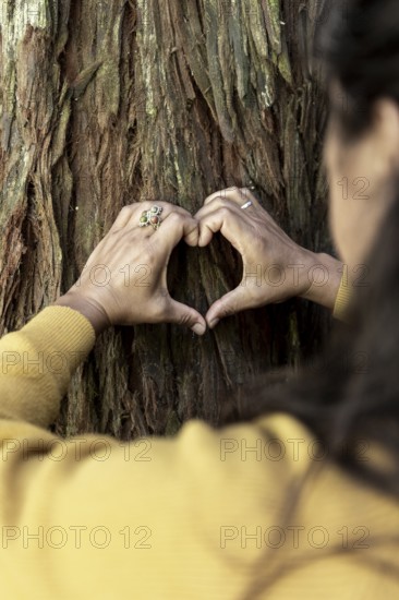 Hands form a heart shape against a textured tree trunk, symbolizing connection and love for nature in Australia. Rings and a yellow sweater add warmth and personality to the scene