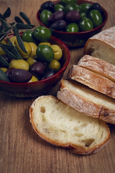A mixture of olives, varieties of Halkidiki, Verdi giganti and Kalamata, in a bowl, with sliced ciabata bread, top view, no people
