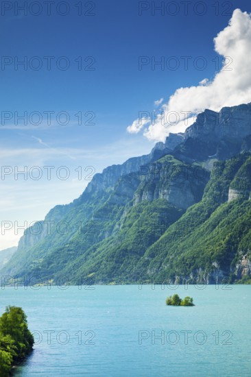 Sunny view over Lake Walen with the small chive island in the turquoise water and mountain range Schären and Leistchamm in the background, Canton St. Gallen, Switzerland