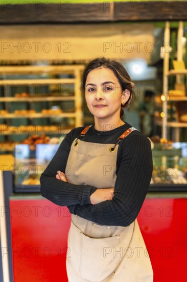 Vertical photo of a latin confident woman worker wearing apron standing proud in a bakery shop