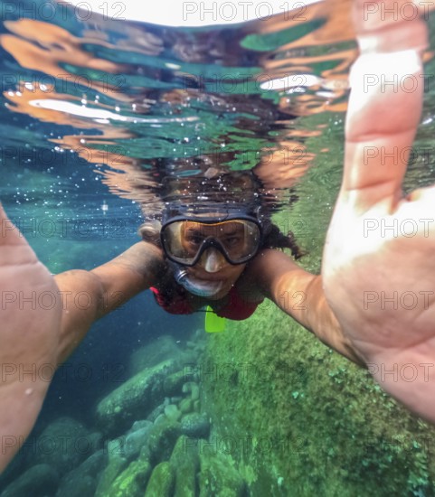 A snorkeler is captured half submerged in the clear waters of Tindaya Beach on Fuerteventura Island, showcasing a selfie shot revealing the underwater rocks and marine life
