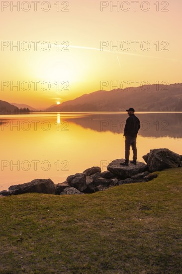 Lonely person standing at the lakeside and watching the sunset, Großer Alpsee, Immenstadt im Allgäu, Bavaria, Germany
