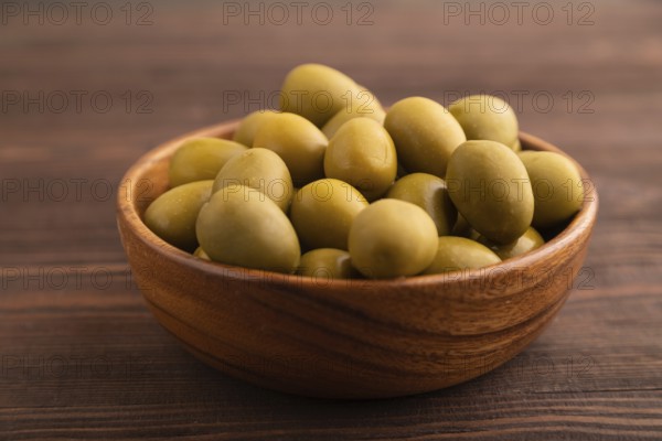 Fresh green olives in wooden bowl on brown wooden background. side view, close up, selective focus