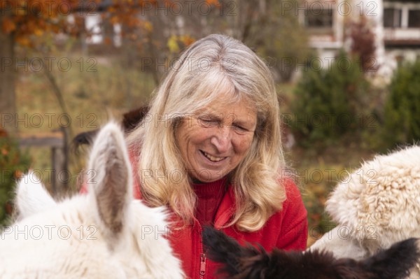 An elderly woman with a warm smile lovingly interacts with her alpacas in the colorful backdrop of the Austrian countryside