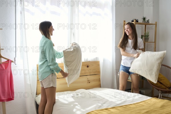 A joyful lesbian couple enjoys a playful pillow fight in a sunlit bedroom The atmosphere is filled with laughter, celebrating love and togetherness within the LGBTQIA+ community