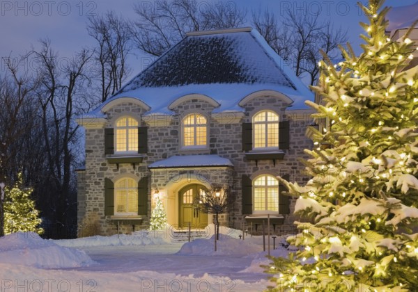 Luxurious residential cottage style home with illuminated evergreen trees at dusk in winter, Quebec, Canada