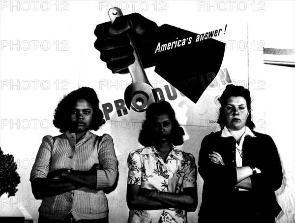 Photograph by Lee. Parachute factory employees stand in front of a propaganda poster for the American company