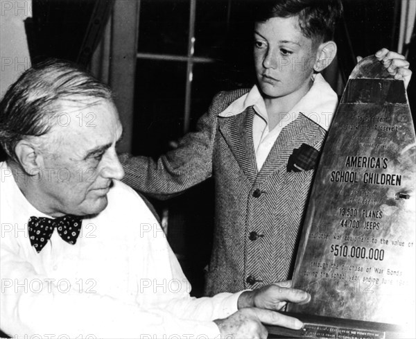 President Roosevelt examining a piece of propeller of a Japanese plane shot down, on which is written the financial participation of school children during the war. The school children's delegate is Donald Buck, aged 13.
