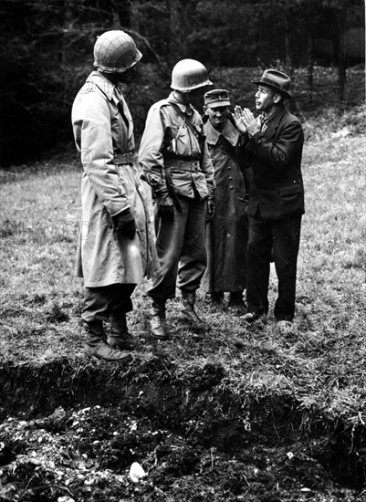 Un nazi se défend devant une fosse commune de victimes des atrocités nazis à Hals (Allemagne). avril 1945