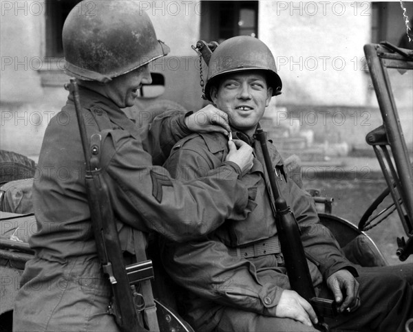 Un caporal américain aide un sous-lieutenant fraîchement nommé à mettre ses galons. (Rambervillers en France, le 2 décembre 1944)