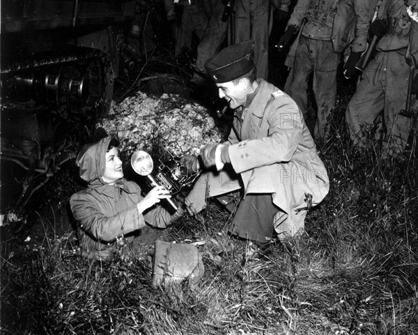 Un Major américain tend un appareil photo à une correspondante de guerre.
(Grande-Bretagne, 1943)