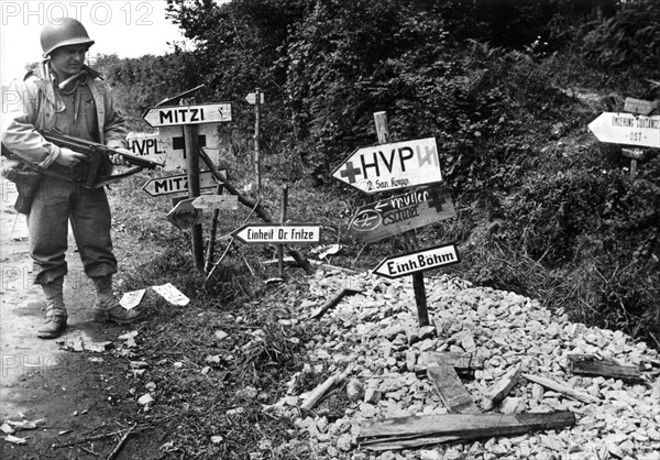 Soldat américain devant les panneaux placés par les Allemands en Normandie, juillet 1944