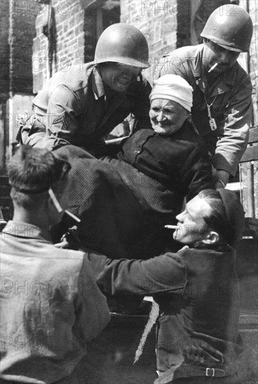 Les soldats américains apportent leur aide à une femme âgée, dans la région de Tessy-sur-Vire.
(Août 1944)