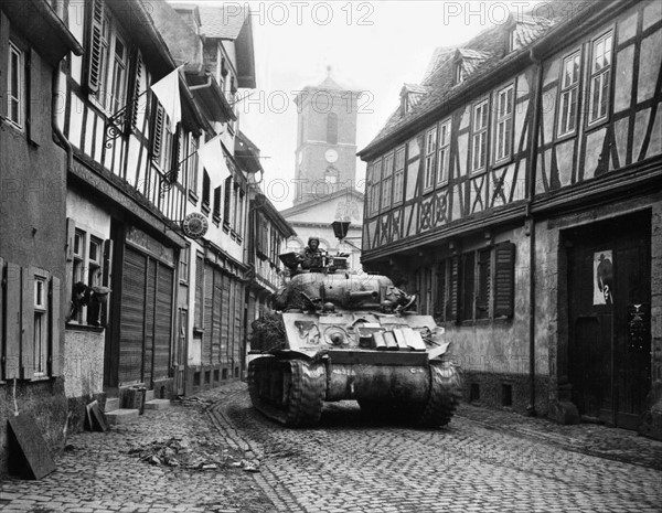 Char américain passant avec fracas sous les drapeaux blancs à Hanau, en Allemagne. 
(28 mars 1945)