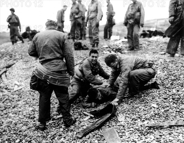 Des soldats américains apportent leur aide à un camarade sur une plage de Normandie. (20 juin 1944)