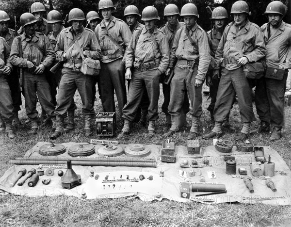 Soldats américains devant un échantillonage de mines allemandes en Normandie. (Juillet 1944)