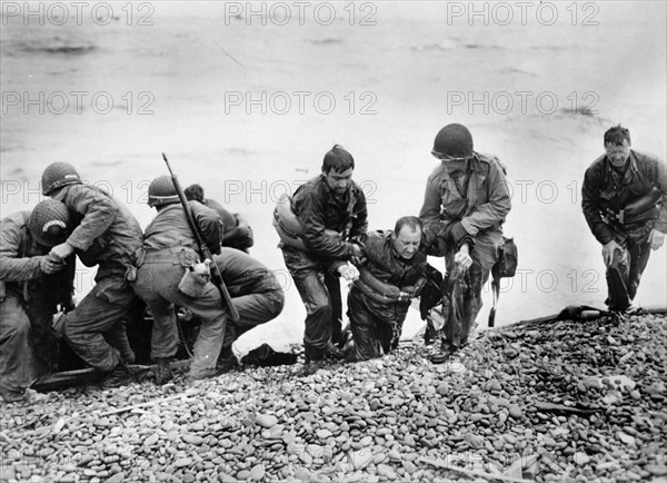 US soldiers carrying their dripping comrades ashore on a Normandy beach (June 1944)