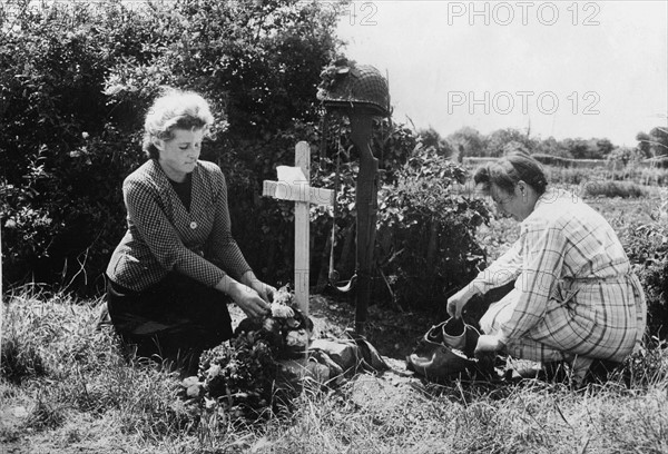 Two inhabitants from Carentan putting flowers on a US soldier's grave