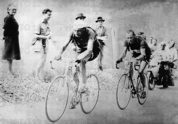Im Windschatten des Italieners Fausto Coppi (l) fährt der Schweizer Hugo Koblet am 18.7.1951 auf dem 14. Tagesabschnitt der Tour de France. Sie nehmen die drei schweren Pyrenäen-Pässe Tourmalet, Aspin und Peyresourde, die eine Gesamtsteigung von rund 3.500 m aufweisen. Koblet verliert durch einen Reifenschaden anderthalb Minuten auf Coppi, holt diesen Vorsprung aber wieder auf und gewinnt am Ende die Etappe. Mit diesem Erfolg setzt er sich auch an die Spitze der Gesamtwertung. Koblet gewinnt am Ende auch die über 24 Etappen führende Tour über 4474 km nach 142:20:14 h.