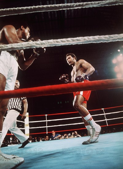 Muhammad Ali (l.) fixiert von Seilen aus in der sechsten Runde des Weltmeisterschaftskampfes am 30. Oktober 1974 in Kinshasa (Zaire) seinen in der Mitte des Ringes stehenden, schon etwas geschwächt wirkenden Gegner George Foreman (r). Mit einem sensationellen K.O.-Sieg in der achten Runde holt sich Ali den Titel des Boxweltmeisters im Schwergewicht zurück. Damit ist der 32jährige nach Floyd Patterson der zweite Boxer, der es schaffte, den Weltmeistertitel im Schwergewicht zurück zu erobern.