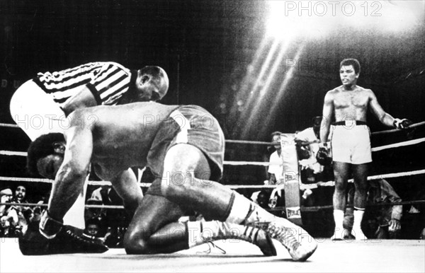 US-Schwergewichtsboxer Muhammad Ali (r, hinten) steht in der 8. Runde in der neutralen Ecke, sein K.o. geschlagener Kontrahent George Foreman (l, vorn) hat Mühe, wieder auf die Beine zu kommen und wird vom Ringrichter ausgezählt. Ali holt sich mit einem sensationellen K.o.-Sieg gegen den Titelverteidiger am 30.10.1974 in Kinshasa (Zaire) den WM-Titel zurück. Nachdem Ali fast bewegungslos in den Seilen hing und die Angriffe des 25jährigen Titelverteidigers abgewehrt hatte, startet er völlig überraschend eine Offensive und schlägt Foreman mit zwei Links-Rechts-Kombinationen K.o. Damit ist der 32jährige der zweite Boxer, der den WM-Titel im Schwergewicht zurückerobert.