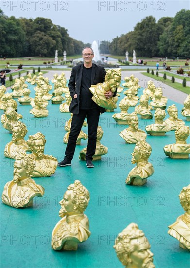 24.08.2018, Bayern, München: Der Nürnberger Künstler Ottmar Hörl blickt neben seiner Kunstinstallation zu Ehren des Märchenkönigs König Ludwig II. im Nymphenburger Schlosspark in die Kamera. 100 Abbilder Ludwigs II. wurden im Rahmen der Kunstinstallation einen Tag vor Ludwigs 173. Geburtstag aufgestellt. Foto: Matthias Balk/dpa | Verwendung weltweit