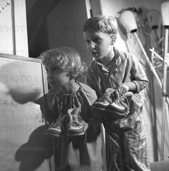 A small girl and a small boy in the pajamas carry their shoes to the door for Saint Nicholas