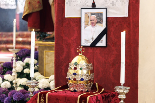 Eine Papstkrone, die sogenannte Tiara, liegt vor einem Bild vom verstorbenen Papst. Zu Ehren des gestorbenen Pontifex wurde der Figur vom Kirchenpatron Petrus am Hauptaltar der Kirche die Papstkrone abgenommen. Dieses Ritual wird immer dann ausgeführt, wenn ein Papst stirbt.