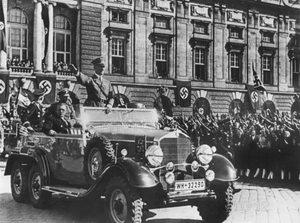 Adolf Hitler grüßt die ihm zujubelnde Menschenmenge in Wien stehend in einem Auto, sitzend neben ihm der österreichische Kanzler Dr. Arthur Seyss-Inquart, aufgenommen am 14. März 1938, einen Tag nach Einmarsch der deutschen Wehrmacht in Österreich. Der Nationalsozialist Dr. Arthur Seyss-Inquart wurde nach dem Rücktritt des österreichischen Kanzlers Kurt von Schuschnigg am 11.3.1938 sein Nachfolger. Unverzüglich forderte er die deutschen Streitkräfte zum Einmarsch in Österreich auf. Dafür berief ihn Hitler zum Reichsstatthalter der Ostmark, wie Österreich jetzt genannt wurde.