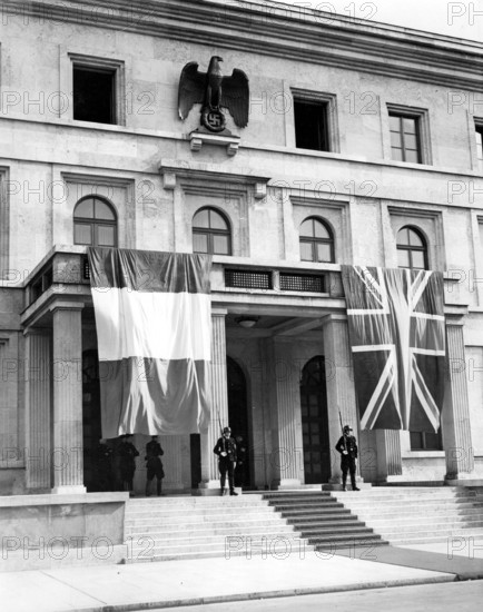 Die französische und die britische Fahne schmücken das Portal des "Führerhauses" am Königsplatz, in dem die Münchner Konferenz stattfindet. Auf dem Treffen zwischen Neville Chamberlain, Edouard Daladier, Benito Mussolini und Adolf Hitler soll versucht werden, den drohenden Krieg des Deutschen Reiches gegen die Tschechoslowakei abzuwenden. Im Münchner Abkommen wird die Abtretung des Sudetenlandes an Deutschland festgelegt.