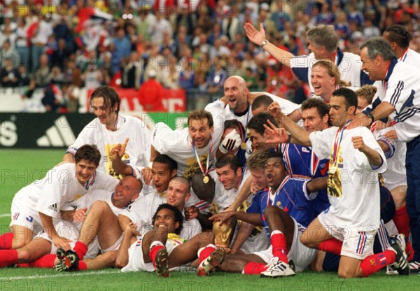 The players of the French national soccer team and their captin Didier Deschamps (C, turned away) and French goalgetter and midfielder Zinedine Zidane (C, behind World Cup) group together for a photograph and cheer with the World Cup trophy in front of them during the 1998 Soccer World Cup in Paris, France, 12 July 1998. France wins the game 3-0 against titleholder Brazil and wins the world champion title for the first time.
