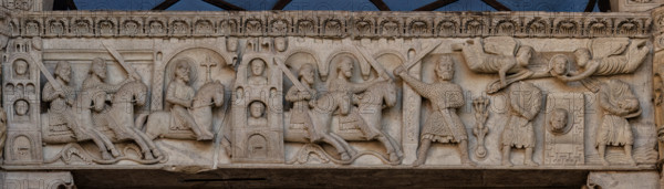 Fidenza, duomo (Cattedrale di San Donnino), facciata, portale maggiore: dettaglio dell’archivolto con “Storie di San Donnino”.
Donnino prosegue la fuga verso Piacenza che gli chiude le porte, poi verso un'altra città finché gli sgherri a cavallo lo raggiungono.
Un soldato mozza con la spada la testa del Santo; due angeli la sollevano e la portano in cielo (senza barba); la testa terrena ricompare (con la barba) su una specie di ara; il Santo la prende tra le mani e s'incammina per attraversare il torrente Stirone.
Opera di  Benedetto Antelami e bottega.

[ENG]
Fidenza, duomo (Cathedral of San Donnino), facade, main portal: detail of the archivolt with “Storiee of St. Donnino”.
Donnino prosegue la fuga verso Piacenza che gli chiude le porte, poi verso un'altra città finché gli sgherri a cavallo lo raggiungono;
Un soldato mozza con la spada la testa del Santo; due angeli la sollevano e la portano in cielo (senza barba); la testa terrena ricompare (con la barba) su una specie di a...