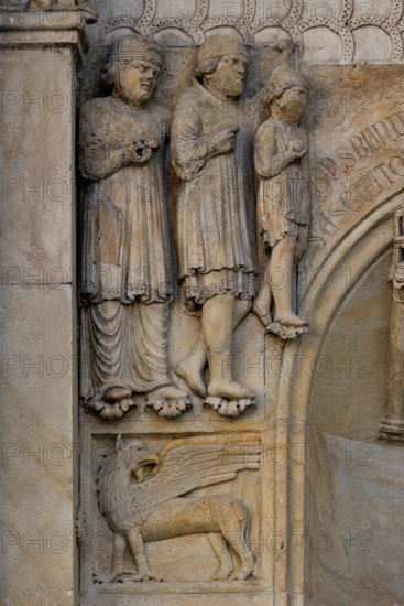 Fidenza, duomo (Cattedrale di San Donnino), sculture tra il portale maggiore e quello di sinistra vicino alla nicchia con il “Re David” di Benedetto Antelami.
Particolare con le figura di un grifo sormontata dal bassorilievo raffigurante verosimilmente una famiglia di pellegrini ricchi in viaggio per Roma. 

[ENG]
Fidenza, cathedral (Cathedral of San Donnino), sculptures between the main portal and the left one near the niche with the “King David” by Benedetto Antelami.
Detail with the figure of a griffin surmounted by the bas-relief probably depicting a family of rich pilgrims traveling to Rome.
Cattedrale di San Donnino, Fidenza (PR), Emilia-Romagna, Italia - Italy