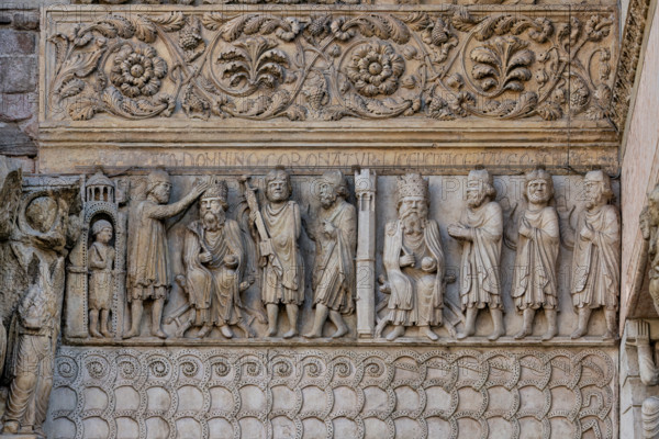Fidenza, duomo (Cattedrale di San Donnino), sculture tra il portale maggiore e quello di sinistra vicino alla nicchia con il “Re David” di Benedetto Antelami.“Storie di San Donnino” con il primo e secondo episodio: Nel pannello a sinistra, la scena è rappresentata all’esterno d’un edificio sotto il quale si trova una guardia armata. 
Donnino, cubiculario di Massimiano Erculeo, stando alla destra dell’imperatore, gli pone la corona sul capo; alla sinistra di Massimiano il Portaspada dimostra che la scena costituisce un momento dell’esercizio del potere sovrano di giurisdizione, probabilmente nei confronti del personaggio posto all’estrema destra. Nella cornice attigua posta sopra è incisa a lettere capitali l’iscrizione: IR . ABEATO . DOMNINO CORONATVR (Imperator a Beato Domnino coronatur = L’Imperatore è incoronato dal beato Donnino).
Nel pannello a destra la distinzione dalla scena precedente è resa evidente, oltre che dal diverso colore della pietra, da una torre merlata poligonale...