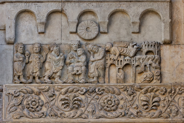 Fidenza, duomo (Cattedrale di San Donnino), sculture tra il portale maggiore e quello di sinistra: “Adorazione dei Magi e sogno di Giuseppe”. Opera di Benedetto Antelami e bottega.
A sinistra si vedono i tre Re Magi che rendono omaggio al Bambino benedicente seduto sulle ginocchia della Madre in maestà; al fianco della Madonna, S. Giuseppe, seduto di profilo, che dorme.
A destra, in un paesaggio caratterizzato dalla presenza di edifici, un angelo raggiunge in volo Giuseppe per parlargli in sogno. All’estrema destra, nella parte inferiore, due colombe in un giardino bevono da una fonte posate su zolle fiorite che raffigurano la terra d’Egitto.
Sui due pannelli in arenaria posti sopra gli altri due, è scolpita una cornice con cinque archetti pensili e sotto quello centrale – sulle teste della Madonna e di Giuseppe – un disco a forma di macina da mulino simboleggia la stella che indicò la via ai Re Magi.
Sugli archetti sono incise a lettere capitali le iscrizioni seguenti: CASPAR . BA...