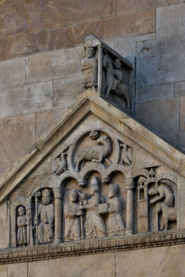 Fidenza, duomo (Cattedrale di San Donnino), portale sinistro, timpano. Nel frontone si leggono, da sinistra, tre scene: L'imperatore Carlo Magno, con un armigero alla sua destra;
Papa Adriano II che porge all'arciprete di San Donnino la mitria e il pastorale (simboli della dignità episcopale); il miracolo dell'ammalato guarito (miracolo compiuto da San Donnino).
Nell’acroterio sul timpano, é raffigurato un personaggio, probabilmente Oberto II Pallavicino condottiero posto da Federico II di Svevia alla guida della città dal 1249 al 1268.

Opera di Benedetto Antelami e bottega.

[ENG]
Fidenza, duomo (Cathedral of San Donnino), left portal, tympanum. In the pediment, from the left, three scenes can be read: Emperor Charlemagne, with a man-at-arms to his right;
Pope Adrian II who offers the archpriest of San Donnino the mitre and the pastoral staff (symbols of episcopal dignity); the miracle of the healed sick man (miracle performed by San Donnino).
In the acroterion on the tympan...