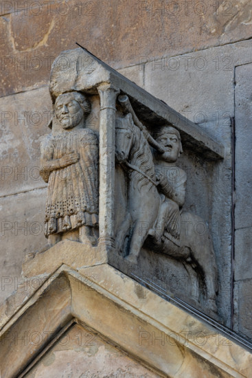 Fidenza, duomo (Cattedrale di San Donnino), portale sinistro, timpano. 
Nell’acroterio sul timpano, é raffigurato un personaggio, probabilmente Oberto II Pallavicino condottiero posto da Federico II di Svevia alla guida della città dal 1249 al 1268. Al suo fianco due suonatori di tromba a cavallo.
Opera di Benedetto Antelami e bottega.

[ENG]
Fidenza, duomo (Cathedral of San Donnino), left portal, tympanum. 
In the acroterion on the tympanum, a character is depicted, probably Oberto II Pallavicino, a leader placed by Frederick II of Swabia at the helm of the city from 1249 to 1268. At his side there are two trumpet players on horseback.
Work by Benedetto Antelami and workshop.
Cattedrale di San Donnino, Fidenza (PR), Emilia-Romagna, Italia - Italy